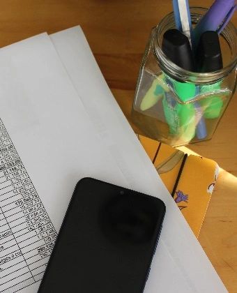 Foto de un balance de elaborado por una gestoría online para autónomos con un teléfono móvil sobre las hojas y rotuladores en un bote de cristal